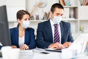 Portrait of two office employees in medical masks concentrating on work with papers and laptop. Necessary precautions during coronavirus pandemic