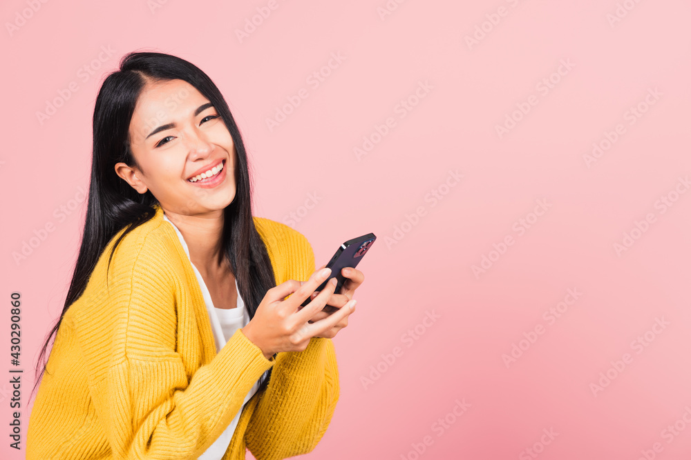 Wall mural Happy Asian portrait beautiful cute young woman excited laughing holding mobile phone, studio shot isolated on pink background, female using funny smartphone making winner gesture