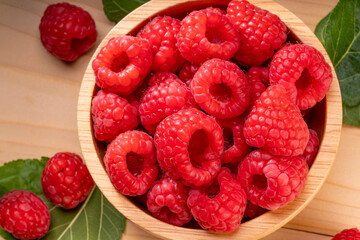 Raspberry fruit in tiny wooden bowl on Wooden background, Raspberries with leaves on Wooden background.
