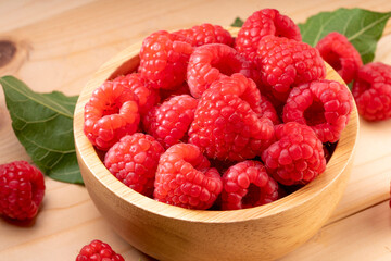 Raspberry fruit in tiny wooden bowl on Wooden background, Raspberries with leaves on Wooden background.