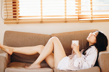 Pretty women with coffee cup lying on sofa light of window