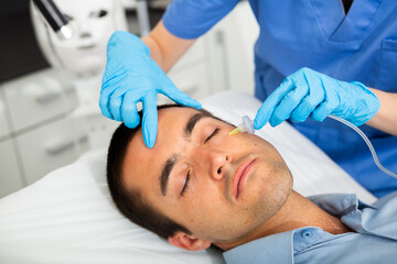 Obraz na płótnie Canvas Young man receiving innovative anti-aging carboxytherapy procedure for facial skin in aesthetic medicine cabinet, infusing of carbon dioxide .
