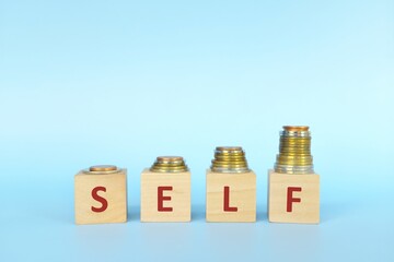 Increasing stack of coins with word self on wooden blocks in blue background. Invest on yourself improvement concept.