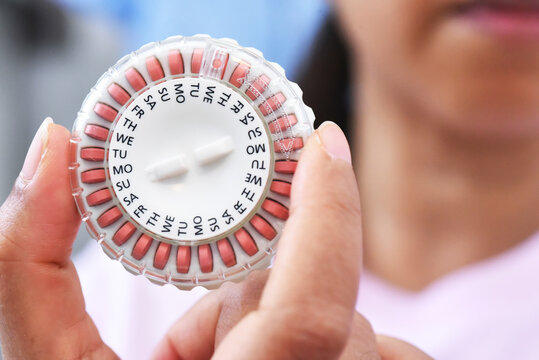 Orange Homone replacement in pill dispenser with date running in woman's hand for treate the Genitourinary syndrome of menopause