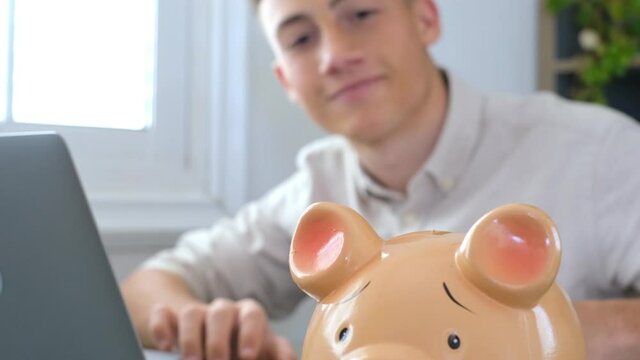Man sit at desk manage expenses, calculate expenditures, pay bills online use laptop, makes household finances analysis, close up focus on pink piggy bank. Save money for future, be provident concept

