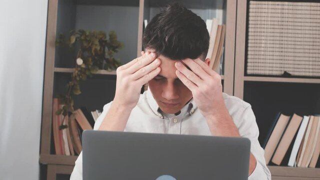 Unhealthy stressed young man suffering headache at home because overwork and studying hard for exams. Tired male teenager doing homework for school
