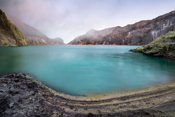 Ijen volcano crater and sulphur mining. Beautiful Landscape mountain and green lake with smoke...