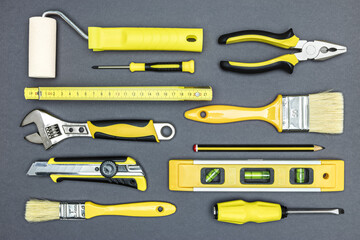 painting tools for house renovation works - paintbrushes and paint roller. construction tools - pliers, adjustable wrench, screwdriver, cutter, folding rule, bubble level. top view on gray background.