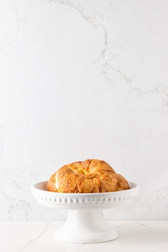 A few croissants in a white cake stand placed on a white marble looking quartz countertop, against a white marble background