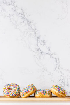 A few donuts covered with colourful sprinkles laying in a wooden tray against a marble looking background made of quartz