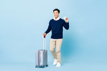 Young smiling handsome Asian tourist man with baggage, passport and boarding pass ready to fly on...