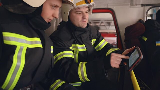 Two firemen analysing data looking on digital tablet in the truck cabin