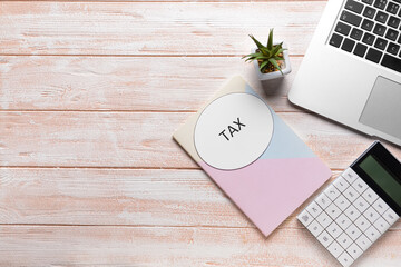Laptop with calculator, notebook and word TAX on wooden background
