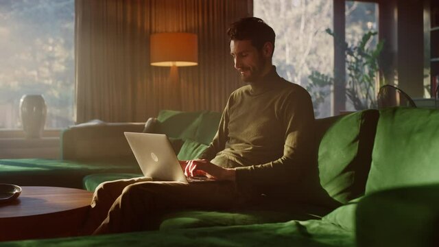 Man Using Laptop at Home, Does Remote Work. Handsome Male Sitting on Sofa Works On Computer, Brainstorms Creative Project, Online Data and Information Research. Productive Work in Sunny Living Room