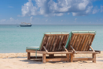 Two wooden deckchairs on a tropical sand beach overlooking the sea water and yacht. Thailand