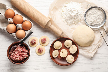 Plate with raw dumplings and ingredients on light wooden background