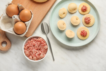 Plate with raw dumplings and ingredients on light background