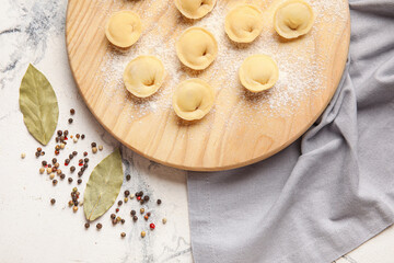 Board with raw dumplings on light background