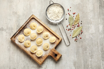 Fototapeta na wymiar Board with raw dumplings, flour and spices on grunge background
