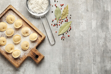 Board with raw dumplings, flour and spices on grunge background