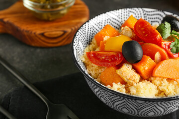 Bowl with couscous and vegetables on dark background