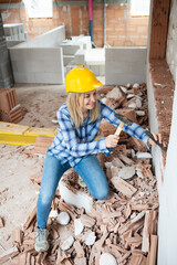 pretty young worker woman with blue work shirt and yellow protective helmet works on construction site and holds hammer in her hand, concept of female worker