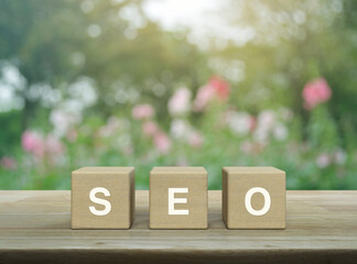 SEO letter on block cubes on wooden table over blur pink flower and tree in garden, Technology...
