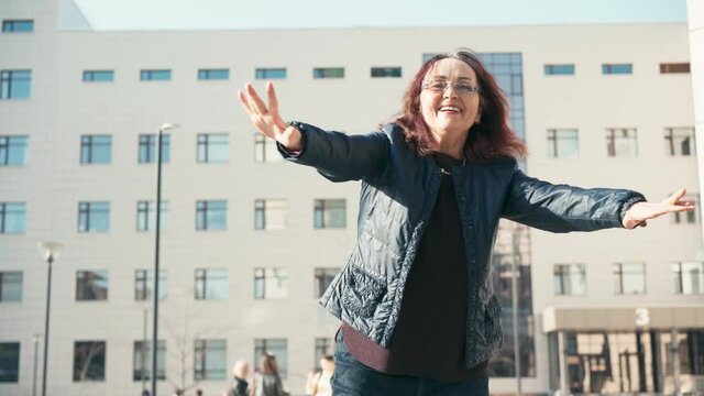 Slow-motion footage of an overjoyed senior woman in glasses dancing in the street on a sunny day.