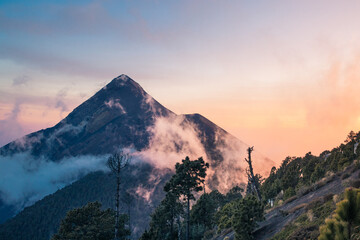 Fototapeta premium beautiful sunset from the camping area of the Acatenango Volcano where you can see the Volcán de Fuego partially covered in fog on a picturesque afternoon with dense forest