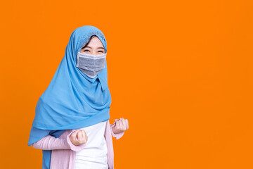 A young Asian Muslim woman wears a surgical mask and shows joy and joy in front of isolate background