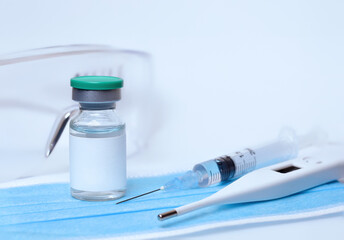 Vial of coronavirus vaccine,medical mask,protective glasses, syringe,thermometer on a white...