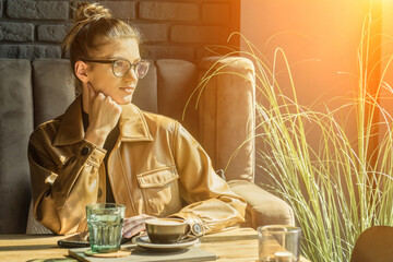 Young woman drinking coffee cup and sitting in cafe. Girl in glasses pauses after work.