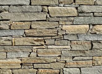 Stone wall made of horizontal shaped  natural rocks. The colors are gray, brown and green with stripes of different colors. Masonry. Background and texture