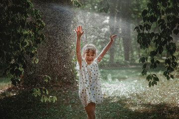 an amiable and laughing girl stands under a watering fountain on a summer day and rejoices