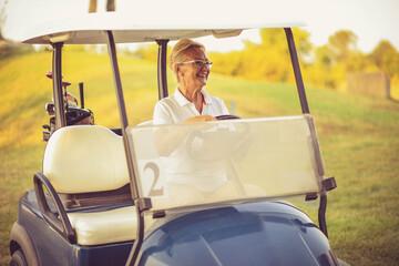 Senior woman riding golf car.