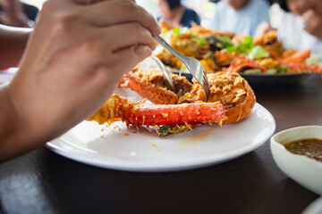 Woman hand holding fork dipping in piece of fried lobster shrimp with garlic on the plate in the restaurant.