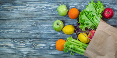 A background of fruits and vegetables peeking out of a paper bag on blue-gray painted wooden planks. Healthy food delivery. Copy space, grocery supermarket banner