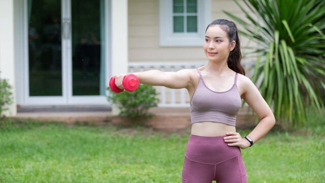 Female fitness instructor exercising with small dumbbell on frontyard.