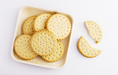 A few cream-filled biscuits on a wooden plate with one broken, delicious dessert, white background