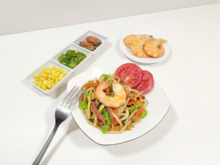 Vegetables, shrimp fried noodles, corn, cucumber, crab; a fork, white background