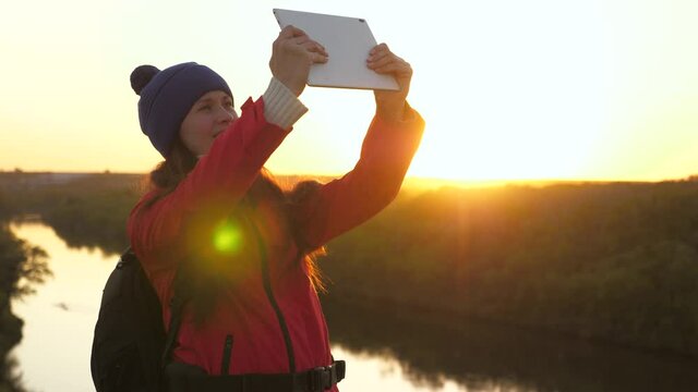 Carefree cheerful girl travels and takes pictures of nature. Young woman tourist blogger records selfie video of peak of mountain using tablet computer against background of beautiful landscape of.
