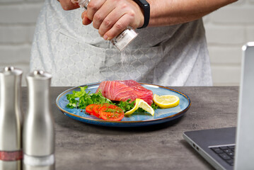Cooking with notebook tuna steak in home kitchen. Online cooking recipe concept, fish cooking at home. lifestyle, healthy eating, cooking and dieting concept.