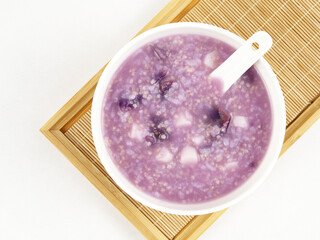 A bowl of purple sweet potato and millet porridge with a spoon on a tray, delicious diet, white background