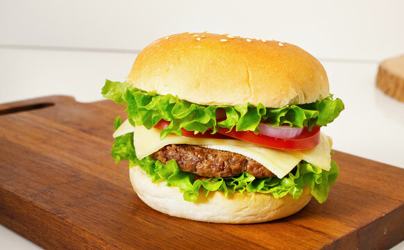 A close-up of a hamburger placed with lettuce, tomato, cheese, beef, onion on a wooden cutting board