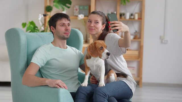 Happy couple take selfie in living room with dog. Spbi woman hold smartphone and smile with man