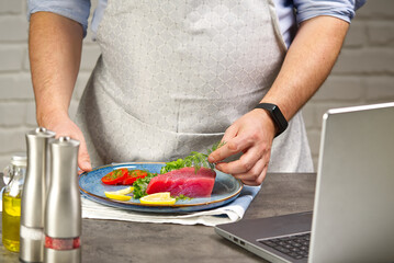 Cooking with notebook tuna steak in home kitchen. Online cooking recipe concept, fish cooking at home. lifestyle, healthy eating, cooking and dieting concept.