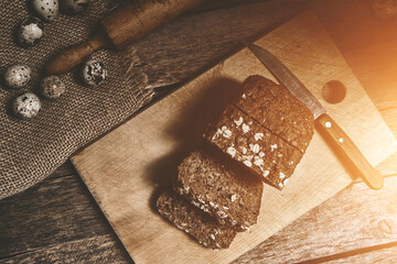 Loaf of sliced grain bread and quail eggs on an old wooden table with bright sunlight.