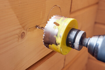 drill with crown making hole in wooden wall for electric cable, socket, switch.