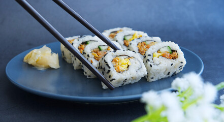 Chopsticks picking up a piece of delicious sushi with eggs and meat floss. Beautiful Japanese cuisine