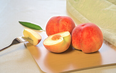 Two fresh peaches whole and a small piece cut on a fork, on wooden cutting board